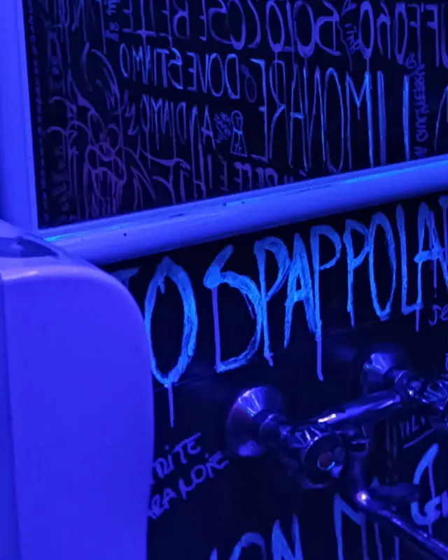 Lo specchio del bagno con le scritte fluorescenti dei clienti, sotto luce UV