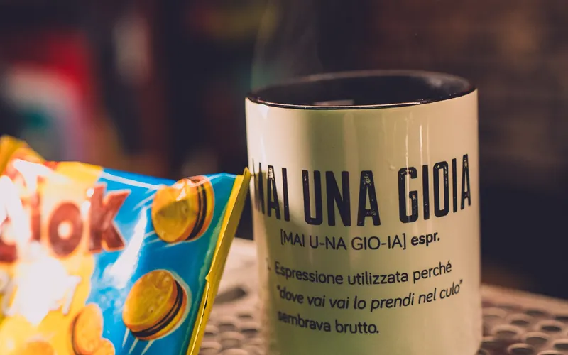 Tazza «Mai una gioia» sul bancone, accanto a un pacchetto di biscotti