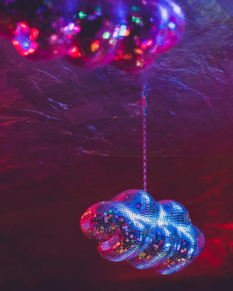 Una nuvola fatta di specchietti da discoteca appesa al soffitto argentato, con riflessi rossi e blu
